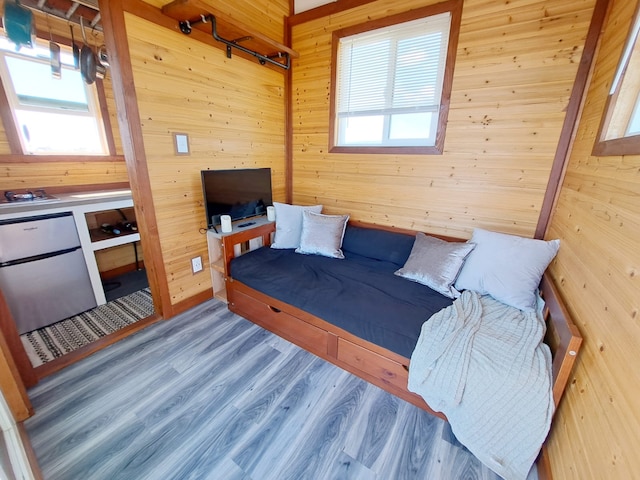 bedroom featuring hardwood / wood-style floors, wooden walls, and stainless steel fridge