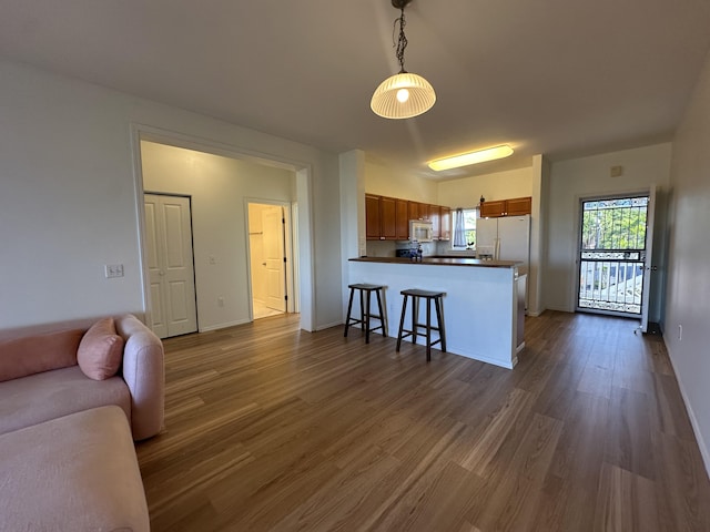 kitchen with a breakfast bar area, dark hardwood / wood-style floors, kitchen peninsula, pendant lighting, and white appliances