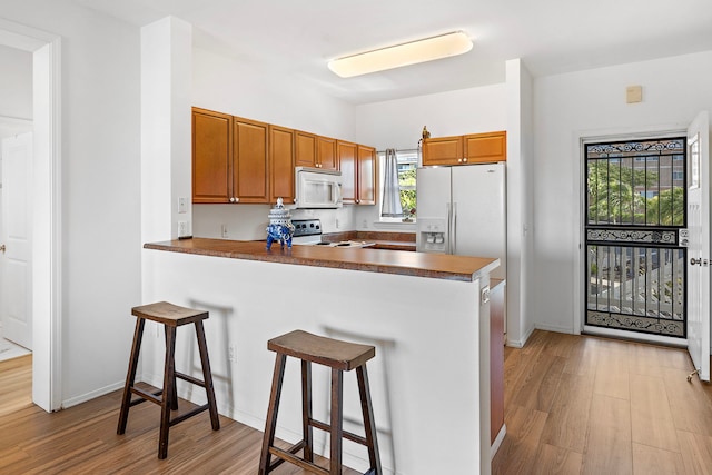 kitchen featuring a kitchen breakfast bar, light hardwood / wood-style floors, white appliances, and kitchen peninsula