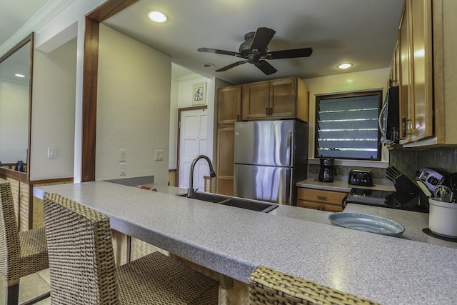 kitchen with appliances with stainless steel finishes, sink, a kitchen bar, ceiling fan, and kitchen peninsula