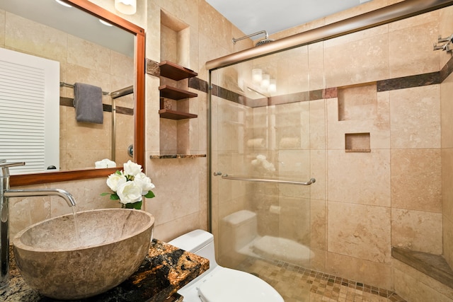 bathroom featuring tile walls, sink, a shower with door, and toilet