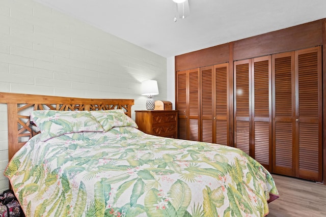 bedroom with two closets, light hardwood / wood-style floors, ceiling fan, and brick wall