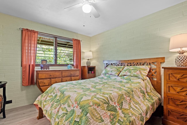 bedroom with ceiling fan, brick wall, and light wood-type flooring