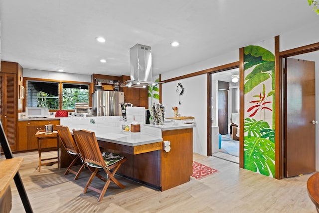 kitchen featuring stainless steel refrigerator, ceiling fan, island range hood, kitchen peninsula, and light wood-type flooring