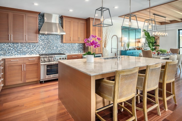 kitchen featuring sink, a kitchen bar, wall chimney range hood, high end stainless steel range, and a center island with sink