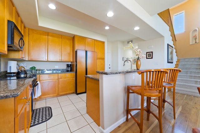 kitchen featuring a center island, dark stone countertops, a breakfast bar, and black appliances