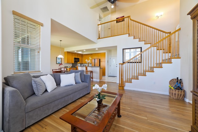 living room with ceiling fan, a towering ceiling, and light hardwood / wood-style flooring