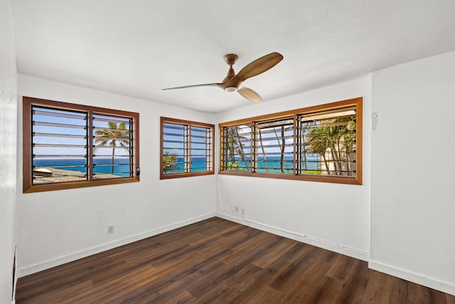 spare room featuring dark wood-type flooring, ceiling fan, baseboards, and a wealth of natural light