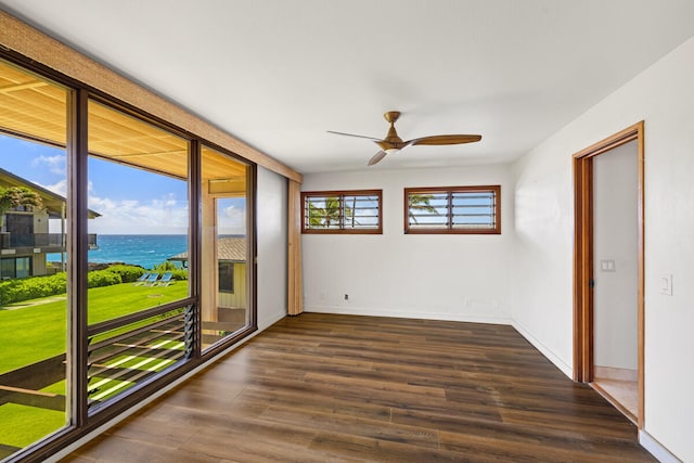 empty room with baseboards, a water view, dark wood-style floors, and a ceiling fan
