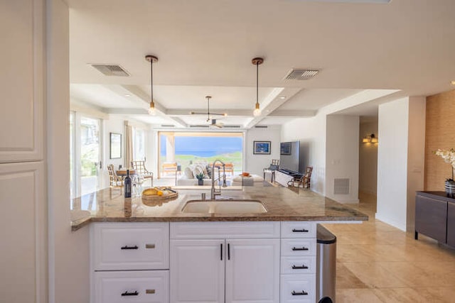 kitchen with stone countertops, visible vents, open floor plan, and a sink