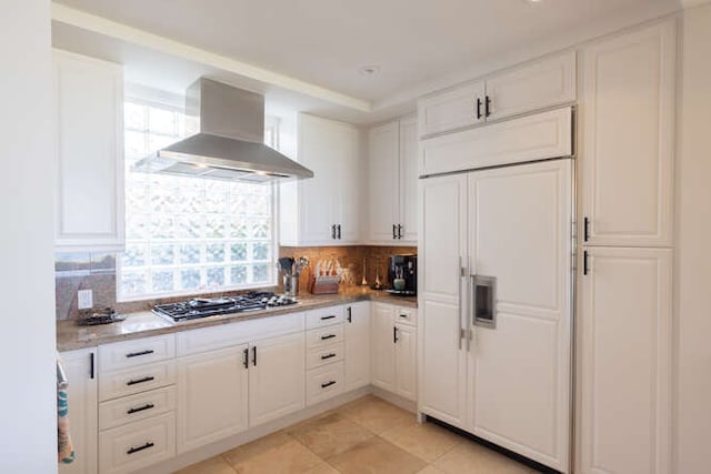 kitchen with paneled built in refrigerator, wall chimney range hood, white cabinets, and stainless steel gas cooktop