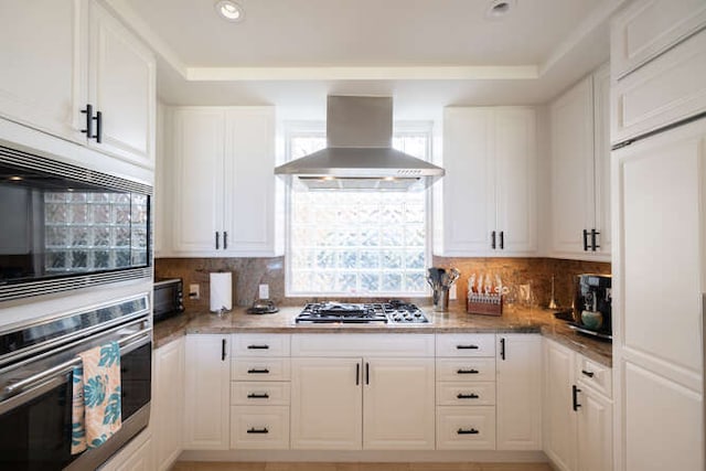 kitchen with stainless steel appliances, white cabinetry, backsplash, and island range hood