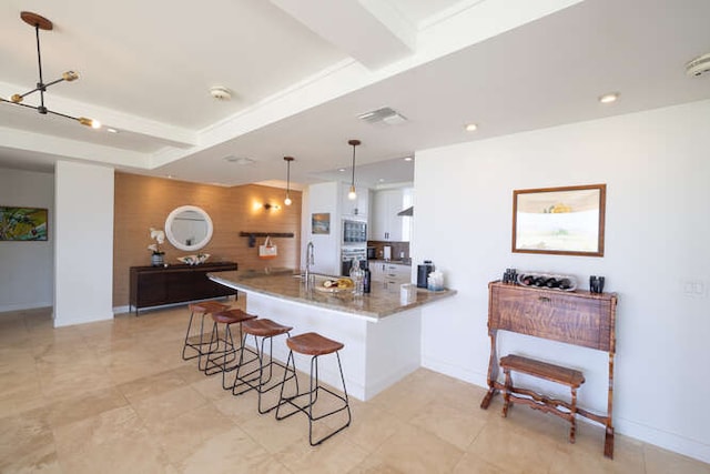 kitchen featuring visible vents, a kitchen breakfast bar, decorative light fixtures, a peninsula, and white cabinetry