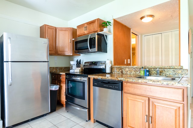 kitchen featuring stainless steel appliances, light stone countertops, sink, and light tile patterned floors