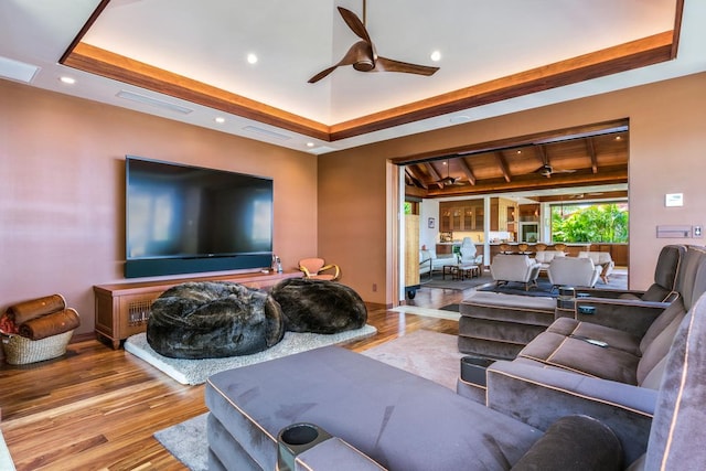 living room with a raised ceiling, ceiling fan, and light hardwood / wood-style flooring