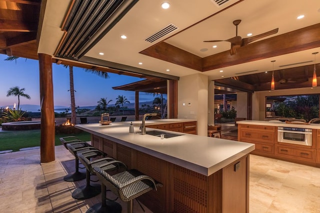 patio terrace at dusk featuring ceiling fan and an outdoor wet bar