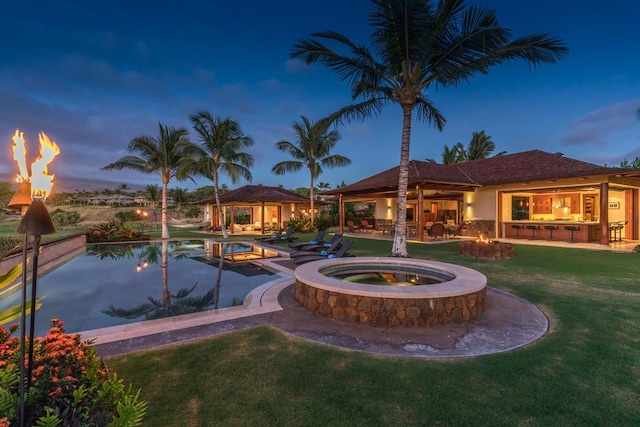 pool at dusk with area for grilling, an in ground hot tub, an outdoor bar, an outdoor fire pit, and a gazebo