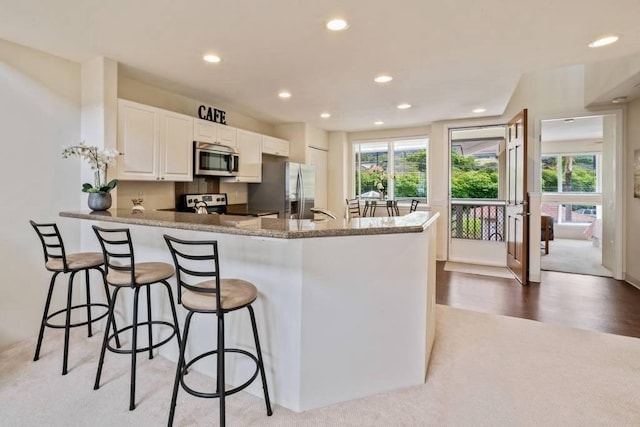 kitchen with plenty of natural light, appliances with stainless steel finishes, kitchen peninsula, light stone countertops, and white cabinets