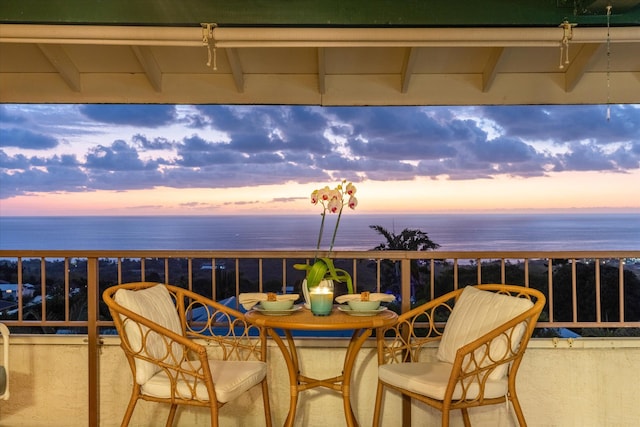 balcony at dusk featuring a water view