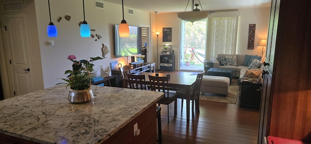 kitchen with hanging light fixtures, a center island, light stone countertops, and dark wood-type flooring