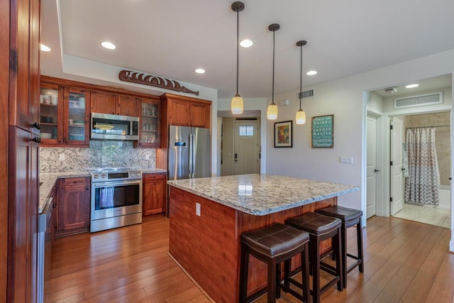 kitchen with light stone counters, dark hardwood / wood-style floors, a kitchen island, stainless steel appliances, and decorative backsplash