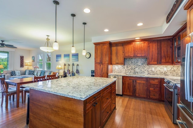 kitchen with tasteful backsplash, hanging light fixtures, a kitchen island, stainless steel appliances, and light stone countertops