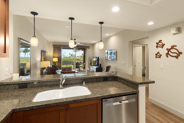 kitchen with decorative light fixtures, dishwasher, sink, dark stone counters, and light wood-type flooring