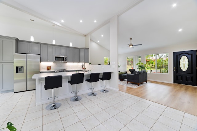 kitchen with light tile patterned floors, gray cabinets, a breakfast bar area, appliances with stainless steel finishes, and decorative backsplash