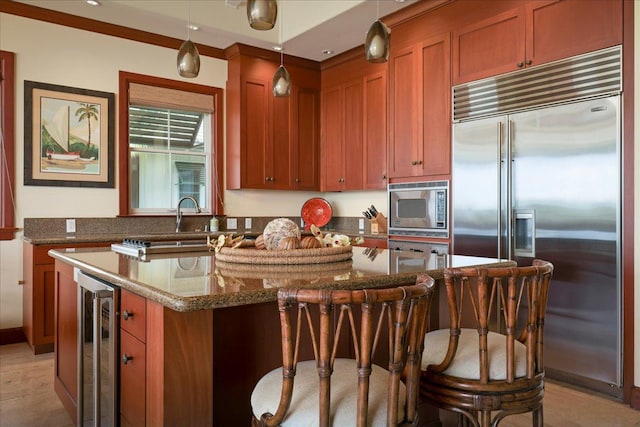 kitchen featuring hanging light fixtures, built in appliances, wine cooler, a kitchen island, and dark stone counters