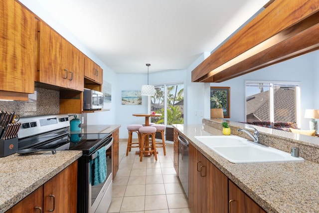 kitchen featuring brown cabinets, hanging light fixtures, stainless steel appliances, a sink, and light tile patterned flooring