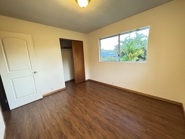 unfurnished bedroom with dark wood-type flooring, a closet, and baseboards