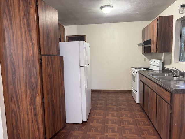 kitchen featuring dark countertops, a sink, a textured ceiling, white appliances, and under cabinet range hood