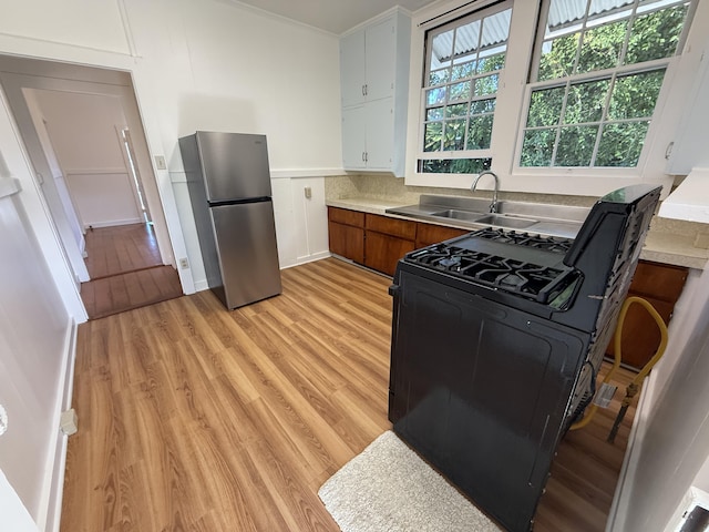 kitchen featuring sink, white cabinets, black range with gas stovetop, stainless steel fridge, and light hardwood / wood-style floors