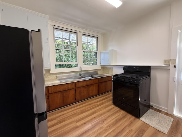 kitchen featuring black gas range oven, sink, light hardwood / wood-style floors, and stainless steel refrigerator