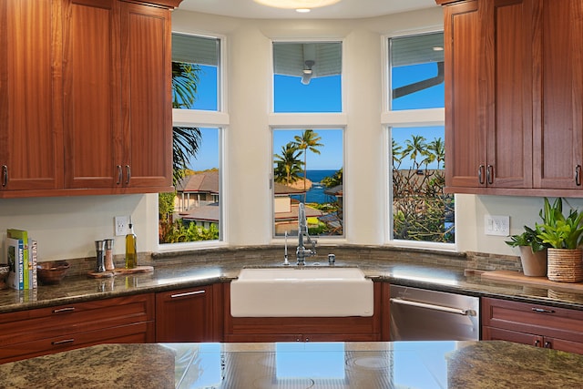 kitchen featuring dark stone countertops, stainless steel dishwasher, a water view, and a sink