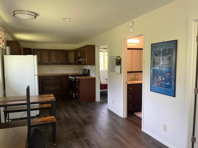 kitchen featuring freestanding refrigerator, dark brown cabinets, dark wood-style flooring, and stainless steel range with gas cooktop