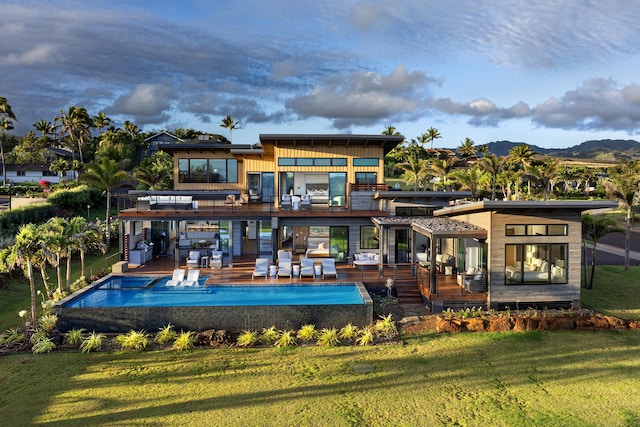 rear view of property with a balcony, a deck with mountain view, and a lawn