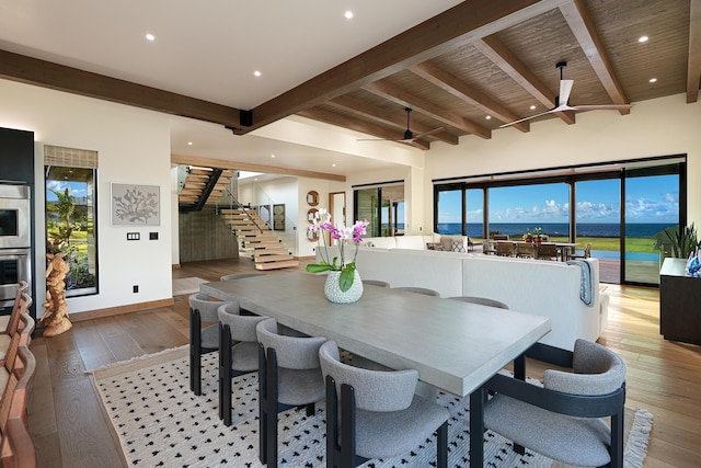 dining area featuring hardwood / wood-style floors, beam ceiling, ceiling fan, and a water view