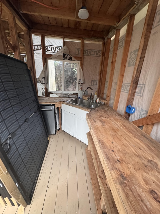 kitchen with butcher block counters, a sink, white cabinets, stainless steel dishwasher, and light wood-type flooring