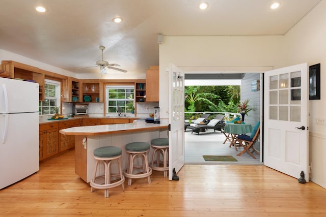 kitchen with a kitchen bar, white fridge, tile counters, light hardwood / wood-style floors, and kitchen peninsula