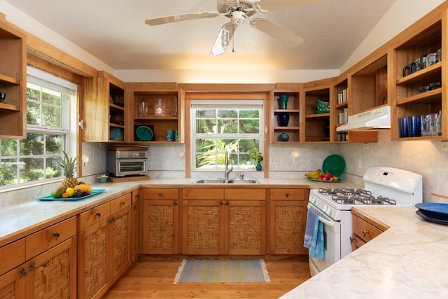 kitchen featuring sink, gas range gas stove, ceiling fan, backsplash, and light wood-type flooring