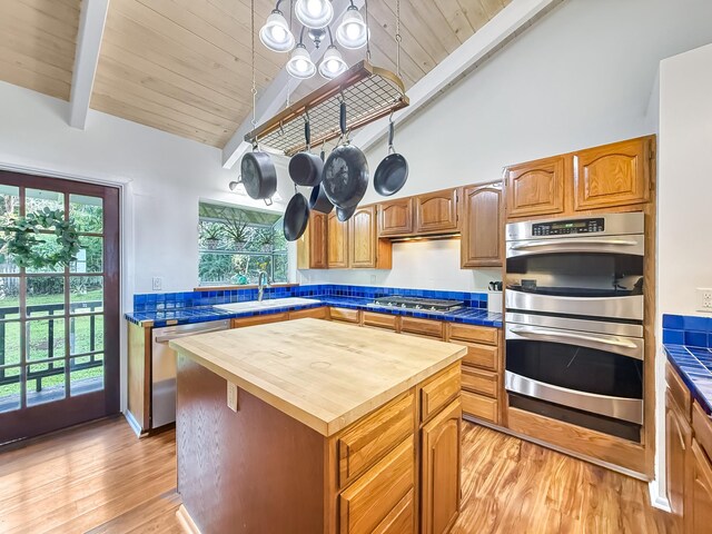 kitchen featuring sink, appliances with stainless steel finishes, a kitchen island, beam ceiling, and light hardwood / wood-style floors