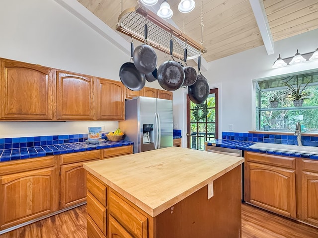 kitchen featuring appliances with stainless steel finishes, beamed ceiling, a center island, tile counters, and light hardwood / wood-style floors