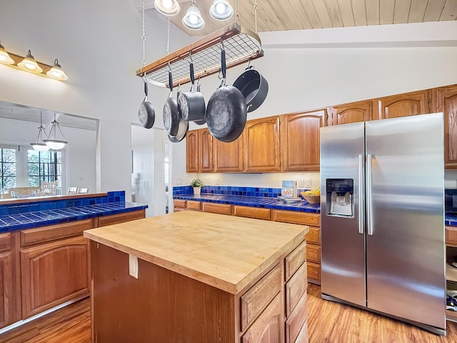 kitchen featuring a kitchen island, decorative light fixtures, tile counters, light hardwood / wood-style floors, and stainless steel fridge with ice dispenser