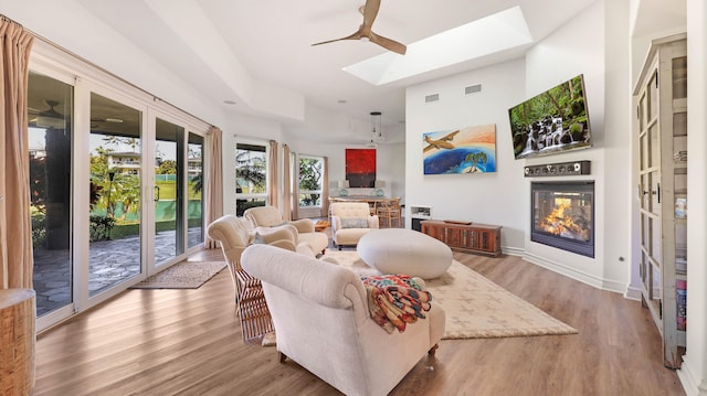 living area featuring a skylight, a glass covered fireplace, visible vents, and wood finished floors