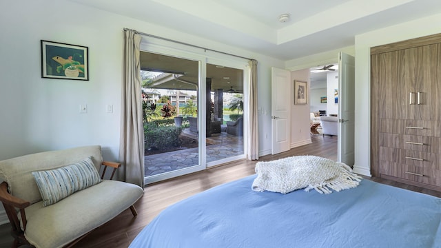 bedroom with baseboards, a raised ceiling, wood finished floors, and access to exterior