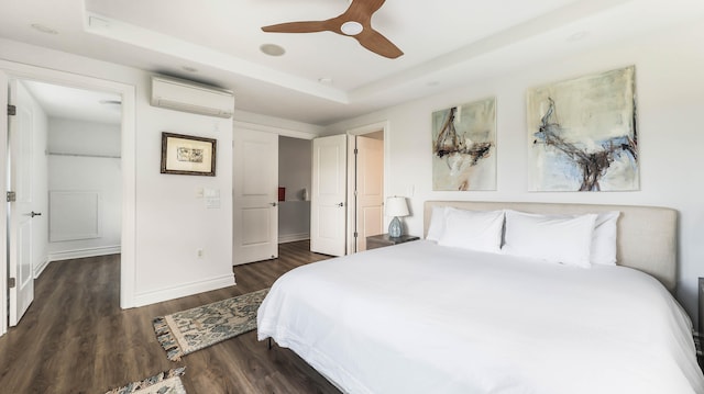 bedroom featuring an AC wall unit, dark wood-style flooring, a raised ceiling, and baseboards