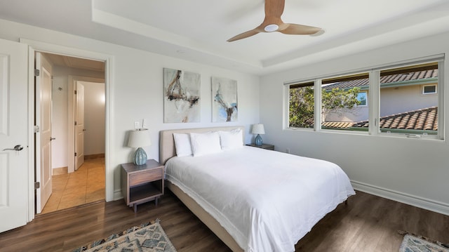 bedroom featuring ceiling fan, a raised ceiling, dark wood finished floors, and baseboards