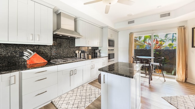 kitchen with visible vents, appliances with stainless steel finishes, white cabinets, wall chimney range hood, and dark stone countertops