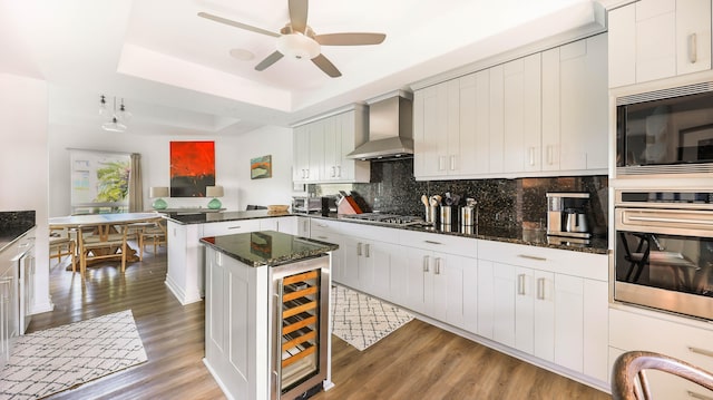 kitchen with wine cooler, a peninsula, appliances with stainless steel finishes, wall chimney exhaust hood, and a raised ceiling